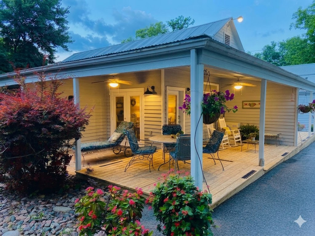 Mountain Laurel cottage wraparound porch at dusk with string lights, lounge chairs, dining table, and colorful hanging flowers
